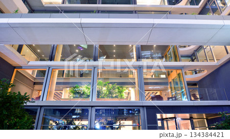 Office building in the evening with lightened workspaces. Modern, glazed skyscraper in financial district. Late hours in the office. Office building in the evening with lightened workspaces. Modern, glazed skyscraper in financial district. Late hours in the office. 134384421