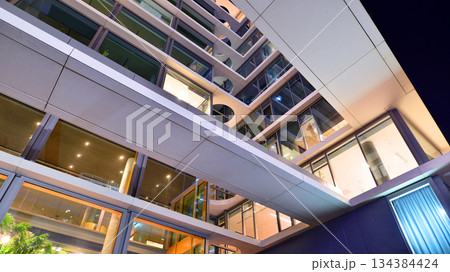 Office building in the evening with lightened workspaces. Modern, glazed skyscraper in financial district. Late hours in the office. 134384424