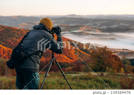 Professional photographer is standing with camera on tripod and shooting majestic view of Carpathian mountains Professional photographer is standing with camera on tripod and shooting majestic view of Carpathian mountains 134384476