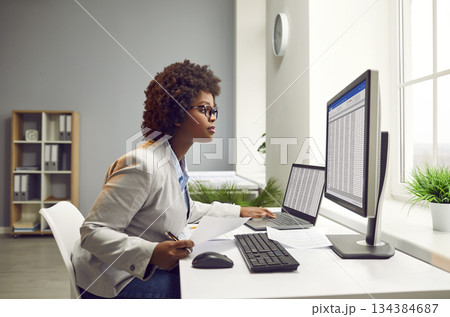 African American accountant working in the office and using business sheets on computers 134384687