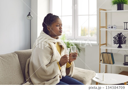 Sick young africanamerican woman feels unwell and is going to drink medicine. 134384709