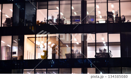 Modern office building in city center illuminated at night. Rows of lit windows against the architectural grid of a modern facade. Concrete and glass facade in its night version. 134385080