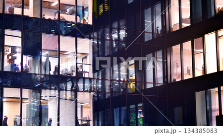 Modern office building in city center illuminated at night. Rows of lit windows against the architectural grid of a modern facade. Concrete and glass facade in its night version. Modern office building in city center illuminated at night. Rows of lit windows against the architectural grid of a modern facade. Concrete and glass facade in its night version. 134385083