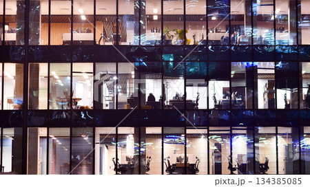 Modern office building in city center illuminated at night. Rows of lit windows against the architectural grid of a modern facade. Concrete and glass facade in its night version. Modern office building in city center illuminated at night. Rows of lit windows against the architectural grid of a modern facade. Concrete and glass facade in its night version. 134385085