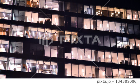 Modern office building in city center illuminated at night. Rows of lit windows against the architectural grid of a modern facade. Concrete and glass facade in its night version. 134385086