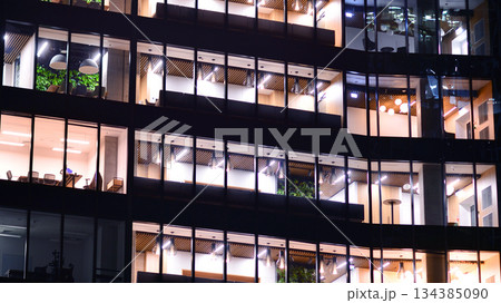 Modern office building in city center illuminated at night. Rows of lit windows against the architectural grid of a modern facade. Concrete and glass facade in its night version. Modern office building in city center illuminated at night. Rows of lit windows against the architectural grid of a modern facade. Concrete and glass facade in its night version. 134385090