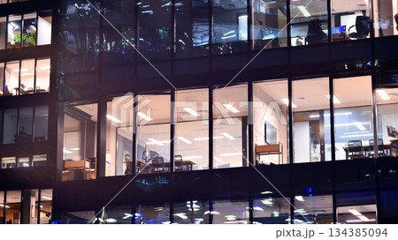 Modern office building in city center illuminated at night. Rows of lit windows against the architectural grid of a modern facade. Concrete and glass facade in its night version. Modern office building in city center illuminated at night. Rows of lit windows against the architectural grid of a modern facade. Concrete and glass facade in its night version. 134385094