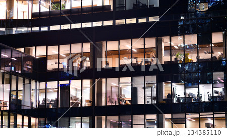 Modern office building in city center illuminated at night. Rows of lit windows against the architectural grid of a modern facade. Concrete and glass facade in its night version. 134385110