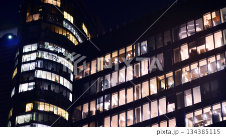 Modern office building in city center illuminated at night. Rows of lit windows against the architectural grid of a modern facade. Concrete and glass facade in its night version. Modern office building in city center illuminated at night. Rows of lit windows against the architectural grid of a modern facade. Concrete and glass facade in its night version. 134385115