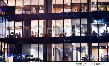 Modern office building in city center illuminated at night. Rows of lit windows against the architectural grid of a modern facade. Concrete and glass facade in its night version. 134385139
