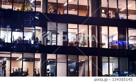 Modern office building in city center illuminated at night. Rows of lit windows against the architectural grid of a modern facade. Concrete and glass facade in its night version. 134385145
