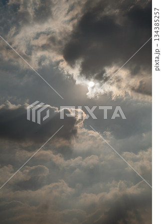 A dramatic cloudscape unfolds, with dark, heavy clouds as bright sunlight pierces through them. 134385257