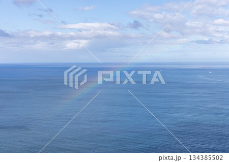 Gentle rainbow over open ocean with pale sunlight drifting clouds and calm water Gentle rainbow over open ocean with pale sunlight drifting clouds and calm water 134385502