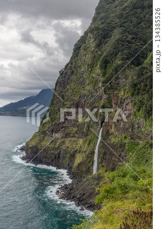 Veu da Noiva waterfall on Madeira drops from green cliffs toward misty Atlantic horizon Veu da Noiva waterfall on Madeira drops from green cliffs toward misty Atlantic horizon 134385526