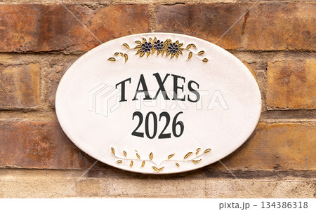 Taxes 2026 new year symbol. Concept words Taxes 2026 on beautiful white sign. Beautiful old brown brick wall background. Business and taxes 2026 new year concept. Copy space. Taxes 2026 new year symbol. Concept words Taxes 2026 on beautiful white sign. Beautiful old brown brick wall background. Business and taxes 2026 new year concept. Copy space. 134386318