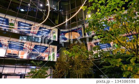 Modern office building in city center illuminated at night. Rows of lit windows against the architectural grid of a modern facade. Concrete and glass facade in its night version. Modern office building in city center illuminated at night. Rows of lit windows against the architectural grid of a modern facade. Concrete and glass facade in its night version. 134386598
