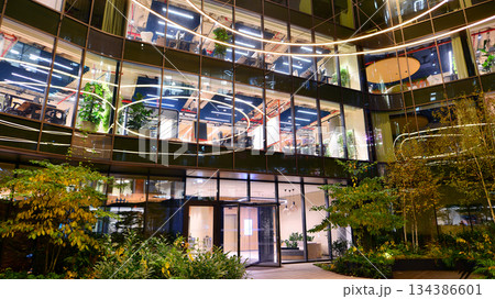 Modern office building in city center illuminated at night. Rows of lit windows against the architectural grid of a modern facade. Concrete and glass facade in its night version. Modern office building in city center illuminated at night. Rows of lit windows against the architectural grid of a modern facade. Concrete and glass facade in its night version. 134386601