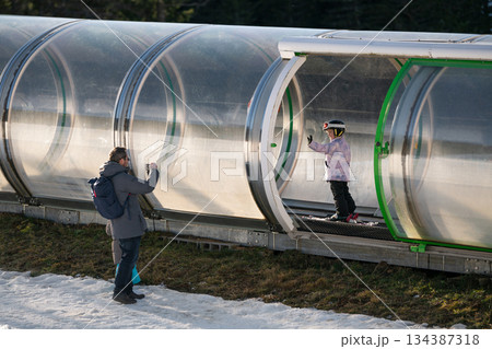A girl on skis stands on a carpet ski lift in a glass tunel 134387318