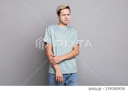 Teenage boy showing disgust and displeasure while reacting to something unpleasant indoors, emotional studio portrait expressing negative feelings, rejection, discomfort and aversion 134388456
