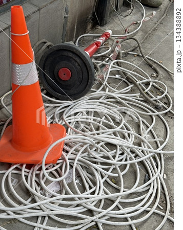 Traffic cone and tangled cables on concrete pavement, urban maintenance and safety concept Traffic cone and tangled cables on concrete pavement, urban maintenance and safety concept 134388892