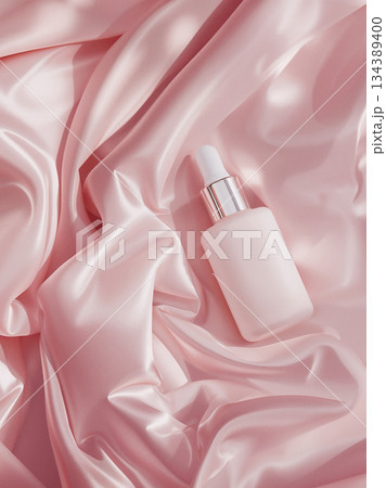 Top view of blank pink serum bottle with dropper on luxurious pink satin fabric background, flat lay mockup for skincare cosmetic product advertisement. 134389400