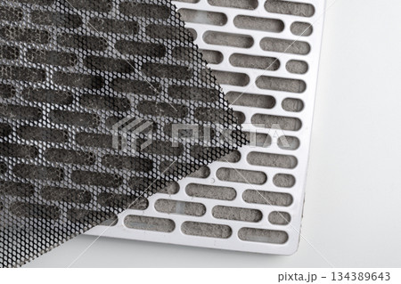 Dusty filter with mesh layer and clogged plastic grille on white table. Air contamination problem concept Dusty filter with mesh layer and clogged plastic grille on white table. Air contamination problem concept 134389643