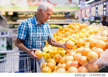 Mature senor examines oranges in fruit section of supermarket Mature senor examines oranges in fruit section of supermarket 134390199