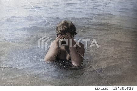 A vintage portrait of a middle-aged woman on the seashore. The woman washes her face with cool seawater. Retro photo from 1971. A vintage portrait of a middle-aged woman on the seashore. The woman washes her face with cool seawater. Retro photo from 1971. 134390822