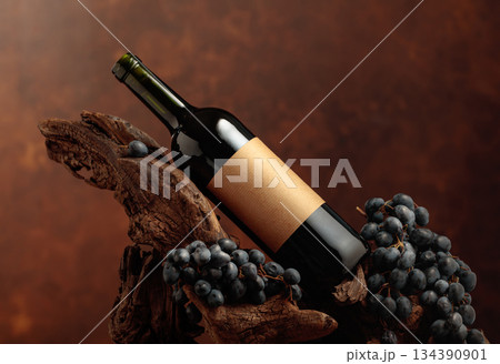 Unopened bottle of red wine, blue grapes, and old snag. 134390901