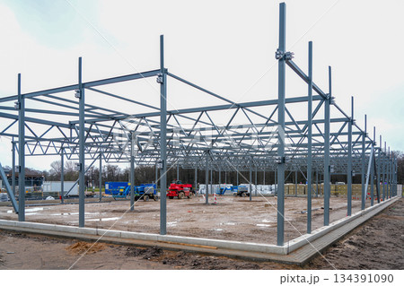 Steel warehouse frame under construction with machinery and materials on industrial building site Steel warehouse frame under construction with machinery and materials on industrial building site 134391090