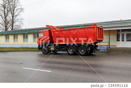 Dump truck sits on the side of the road. Construction equipment is parked near a one-story building. 134391118