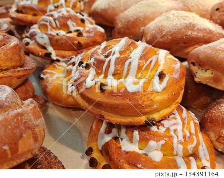Assortment of Fresh Sweet Pastries with Icing and Raisins Close-Up. Close-up of delicious freshly baked sweet buns, cinnamon rolls and donuts with white icing, raisins and powdered sugar.  134391164