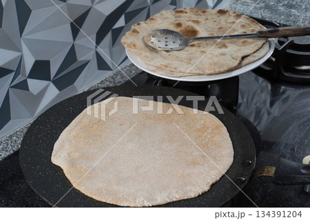 Making an unleavened flatbread the roti. A close-up of the round flatbread being fried on a flat, rimless griddle called a tawa, and several cooked roti on a white plate. Baking homemade bread. Making an unleavened flatbread the roti. A close-up of the round flatbread being fried on a flat, rimless griddle called a tawa, and several cooked roti on a white plate. Baking homemade bread. 134391204