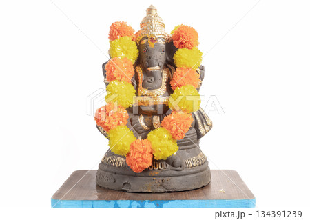 Ganesha idol adorned with a bright orange and yellow floral garland for Hindu worship and celebration. 134391239