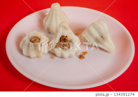 Steamed sweet modak rice dumplings on a white plate against a red background for the Ganesh Chaturthi festival. 134391274