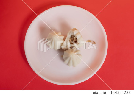 Steamed sweet modak rice dumplings on a white plate against a bright red background 134391288