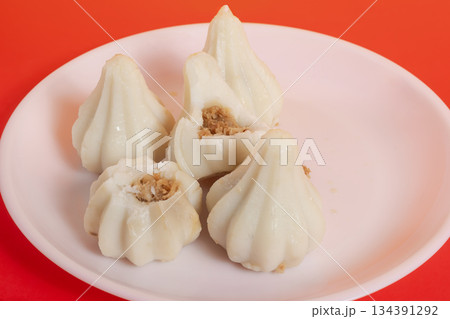 Steamed sweet modak rice dumplings on a white plate against a bright red background Steamed sweet modak rice dumplings on a white plate against a bright red background 134391292