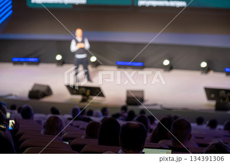 Speaker on stage presenting at conference as audience watches in a large auditorium 134391306
