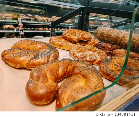 Fresh Baked Bread and Pastries in Bakery Display Case. Assortment of freshly baked bread rolls, pretzels and buns with poppy seeds, sesame and almonds displayed in glass bakery case. Appetizing food p 134391411