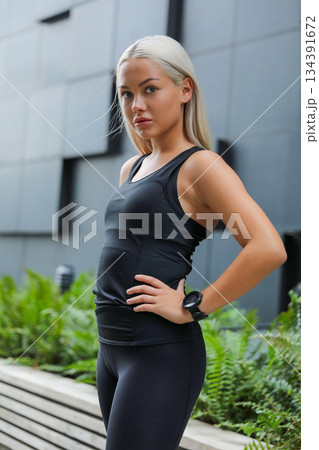 Confident woman in activewear standing outdoors near urban architecture Confident woman in activewear standing outdoors near urban architecture 134391672