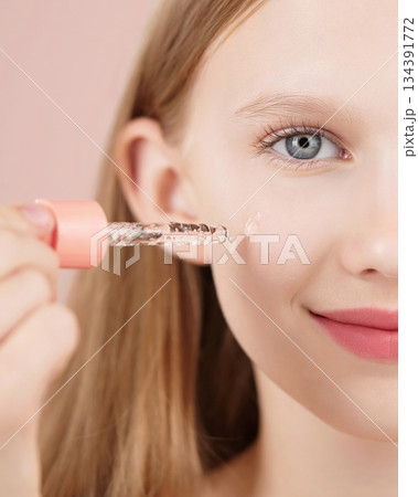 Half face portrait of a funny smiling young girl applying serum on face using an dropper. Blonde Caucasian girl with blue eyes isolated on pink background. Advertising concept skin care for teenagers. Half face portrait of a funny smiling young girl applying serum on face using an dropper. Blonde Caucasian girl with blue eyes isolated on pink background. Advertising concept skin care for teenagers. 134391772