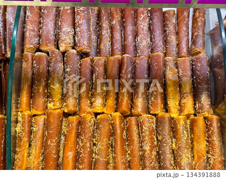 Rolled fruit leather sheets aligned in rows inside a market display case in Istanbul bazaar. Traditional preservation methods, natural sweetness, and simple ingredients reflecting culinary heritage Rolled fruit leather sheets aligned in rows inside a market display case in Istanbul bazaar. Traditional preservation methods, natural sweetness, and simple ingredients reflecting culinary heritage 134391888
