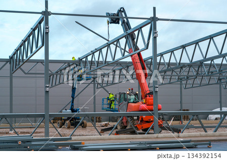 Steel frame construction with crane and aerial lifts during assembly of industrial building structure Steel frame construction with crane and aerial lifts during assembly of industrial building structure 134392154