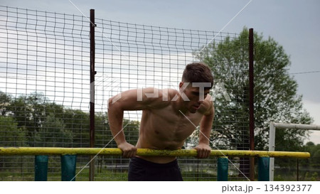 Male shirtless athlete doing push ups on parallel bars at nature. Strong sporty man exercising at sports ground. Young sportsman training hard outdoor. Concept of active sportive lifestyle. Slow mo 134392377