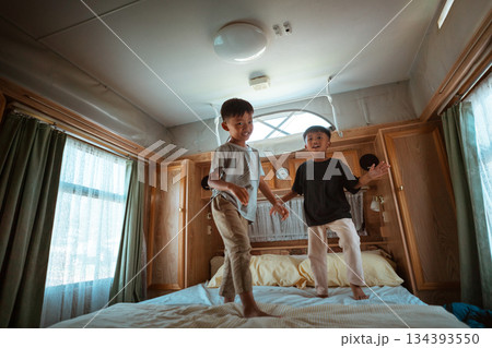 Joyful Kids Energetically Jumping on Bed in a Cozy Bedroom Setting Joyful Kids Energetically Jumping on Bed in a Cozy Bedroom Setting 134393550
