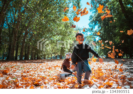 Children are Joyfully Playing and Laughing in Autumn Leaves at the Park Children are Joyfully Playing and Laughing in Autumn Leaves at the Park 134393551