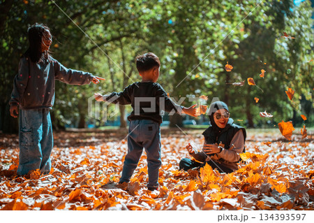 Delightful Children Joyfully Playing Amidst Autumn Leaves in a Sunlit Park 134393597