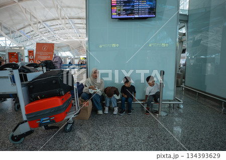 A family waits eagerly at a busy airport terminal with their luggage 134393629