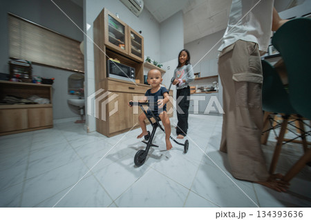 A joyful toddler happily riding a colorful tricycle in a modern kitchen 134393636