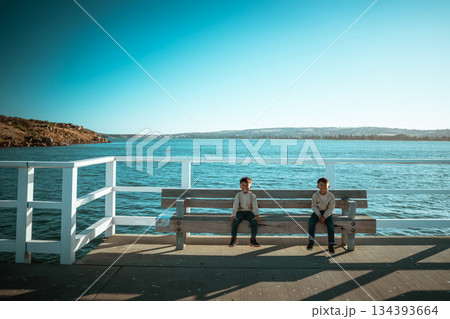 Two Children Happily Sitting by the Water Under a Beautiful, Clear Sky Above Them Two Children Happily Sitting by the Water Under a Beautiful, Clear Sky Above Them 134393664